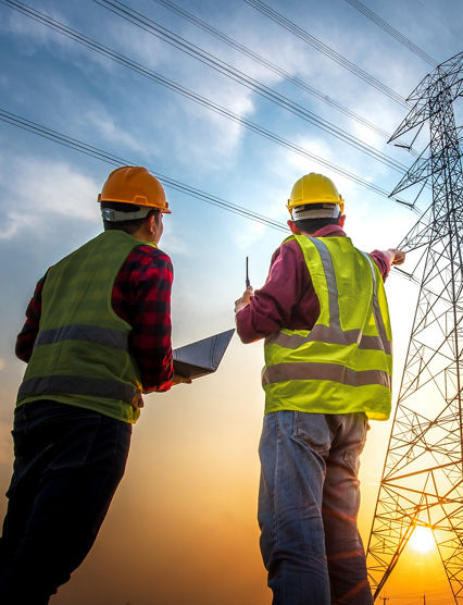 Picture of two electrical engineers using a notebook computer standing at a power station to view the planning work by producing electrical energy at high voltage electrodes.