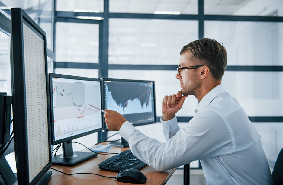 Analysing graphs. Young businessman in formal clothes is in office with multiple screens. Conception of exchange and money.