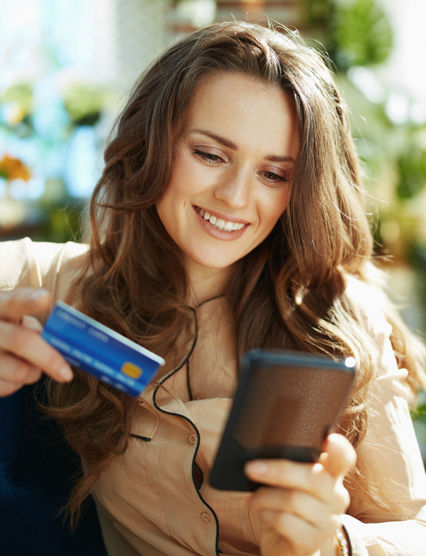 Green Home. happy trendy middle aged woman with long wavy hair with credit card making online shopping on e-commerce website in the modern house in sunny day.