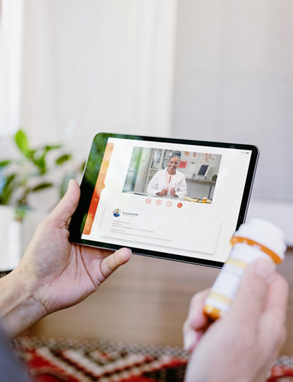 While holding a prescription medication container, an unrecognizable senior man video chats with a female doctor. The man is asking quesitons about his medication.