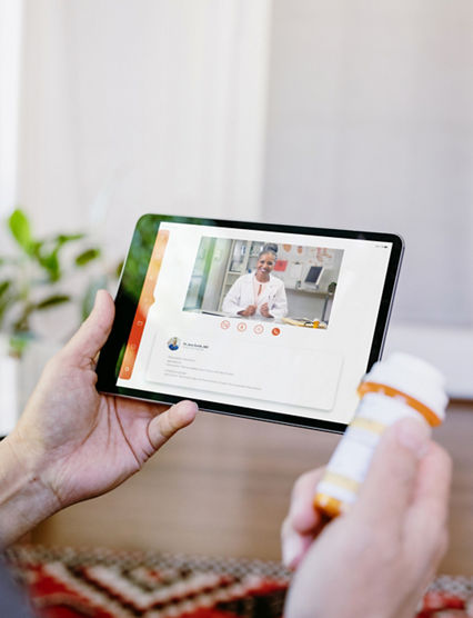 While holding a prescription medication container, an unrecognizable senior man video chats with a female doctor. The man is asking quesitons about his medication.