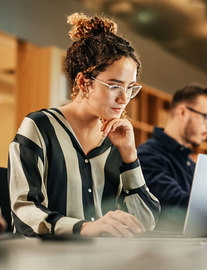 Portrait of Enthusiastic Hispanic Young Woman Working on Computer in a Modern Bright Office. Confident Human Resources Agent Smiling Happily While Collaborating Online with Colleagues.