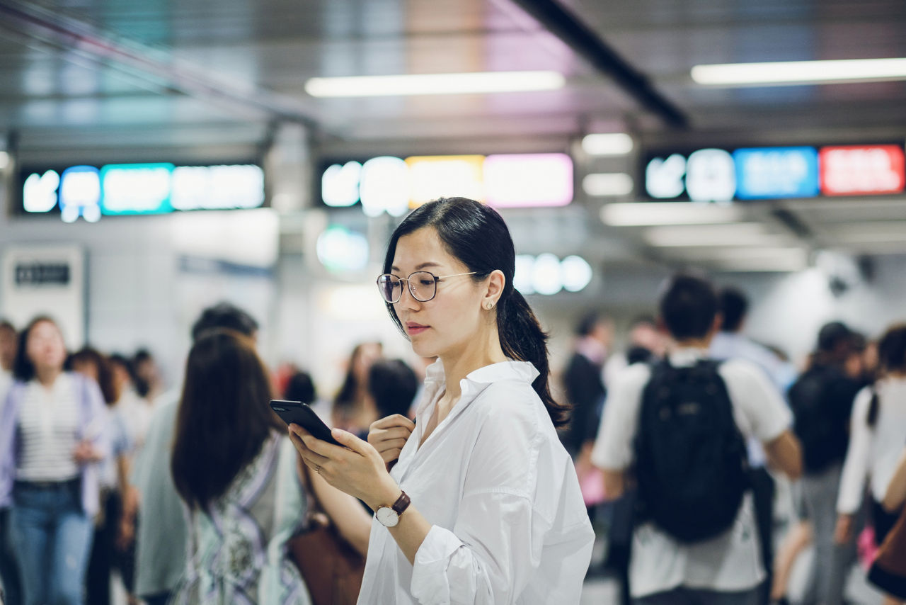 Beautiful young woman using smartphone in subway station during rush hour