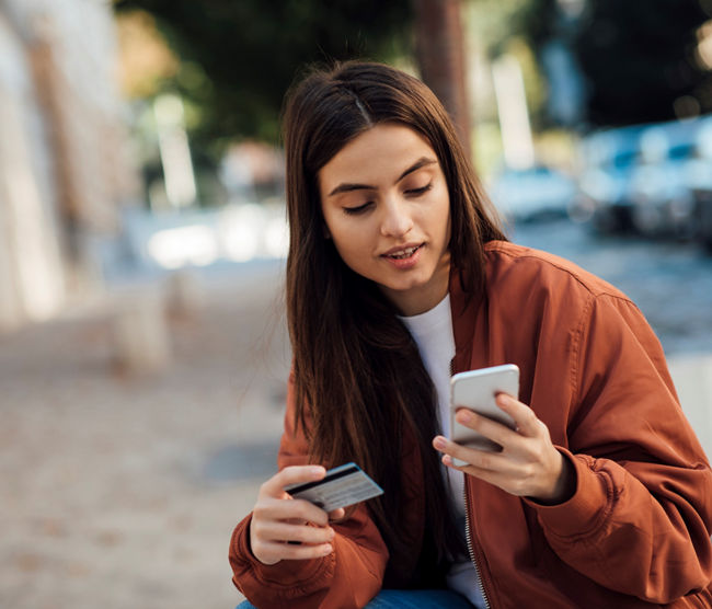 Young girl using credit card and mobile phone outdoore.