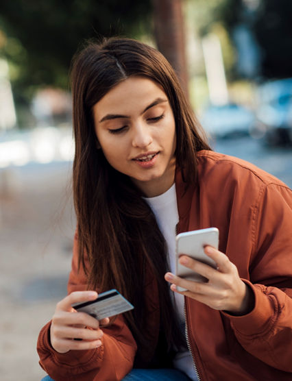 Young girl using credit card and mobile phone outdoore.