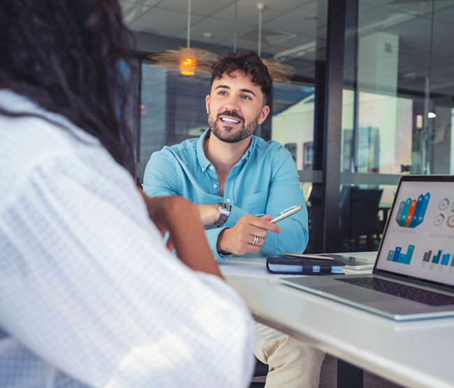 Business colleagues having a conversation. They are discussing a charts and graphs on a laptop computer. They are both young business people casually dressed in an office. Could be an interview or consultant working with a client.