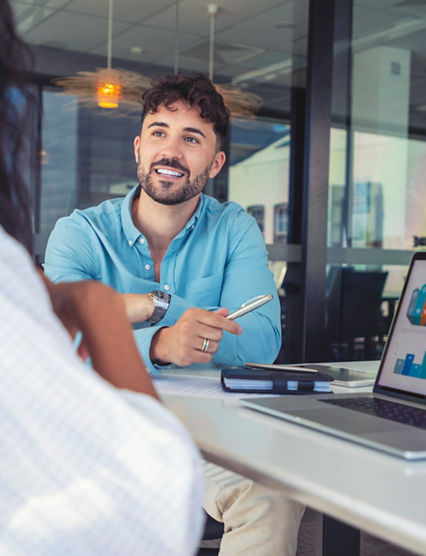 Business colleagues having a conversation. They are discussing a charts and graphs on a laptop computer. They are both young business people casually dressed in an office. Could be an interview or consultant working with a client.