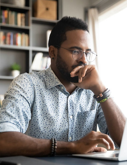 Focused concentrated young african businessman sit at desk look at laptop, serious afro american male professional analyst working online on computer data watch webinar thinking of problem solution