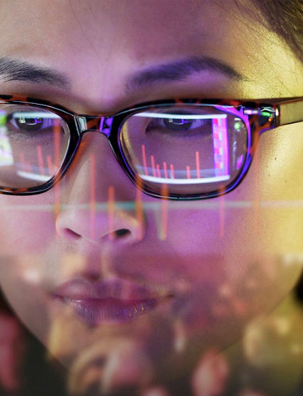 Close up stock photo of an Asian woman carefully studying moving data on her computer screen, the screen is unusual as it is transparent and the camera is looking through the back of the screen.