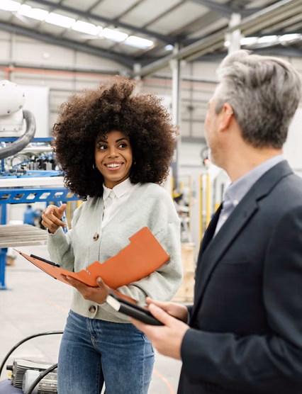 Smiling engineer holding folder discussing with colleague in factory