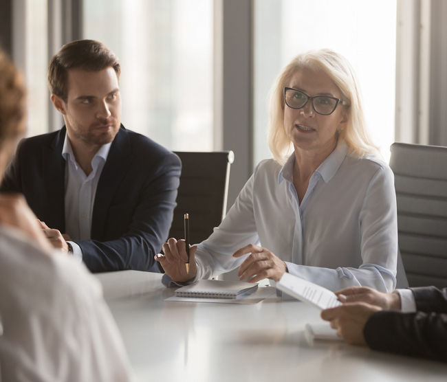 Serious middle aged businesswoman talks at group board executive meeting, confident mature old female leader speaking discussing work offers solution negotiating with partners at corporate briefing