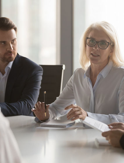 Serious middle aged businesswoman talks at group board executive meeting, confident mature old female leader speaking discussing work offers solution negotiating with partners at corporate briefing