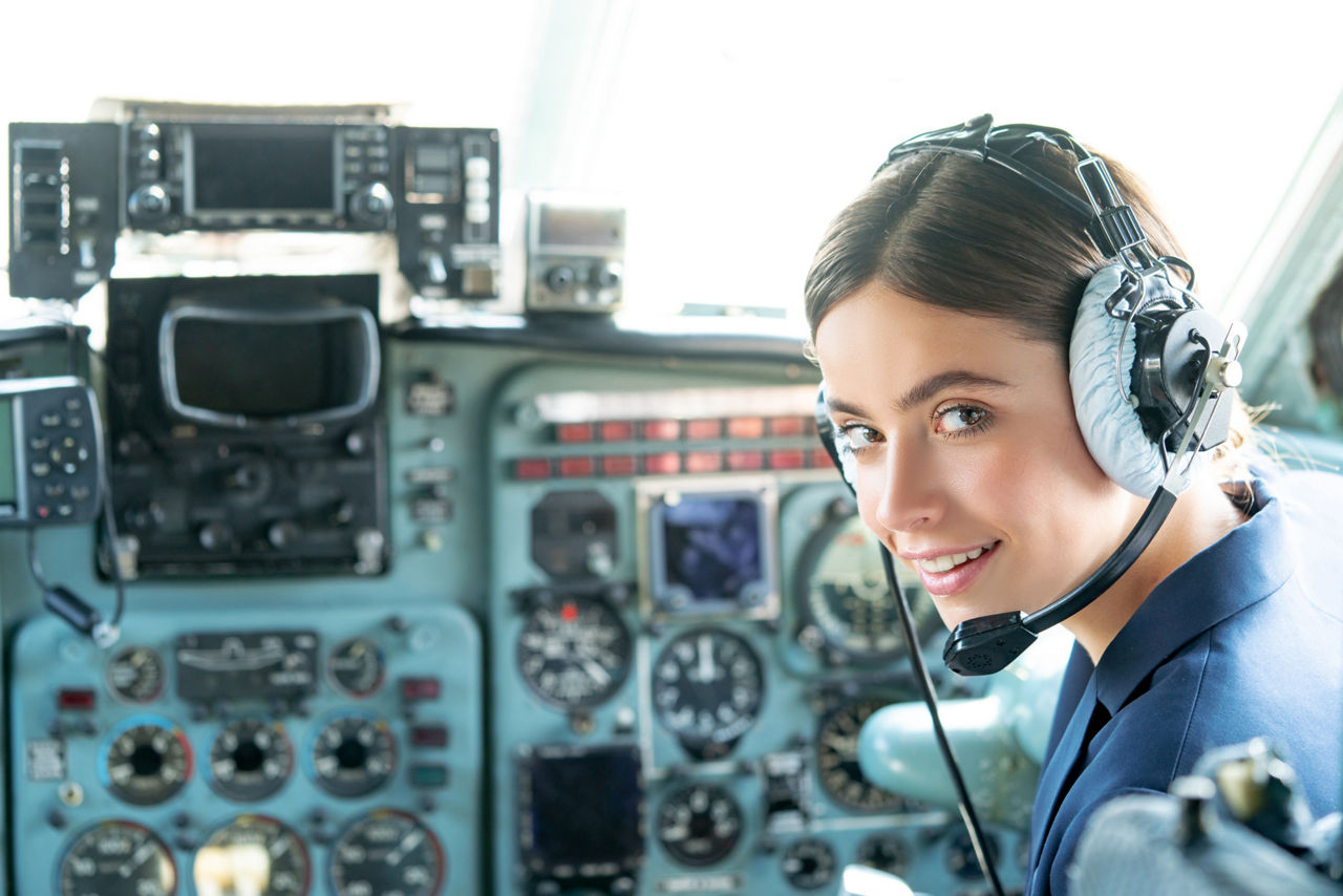 Happy and successful flight. Smiling female pilot in the aircraft , she is holding aviator headset and looking at camera. Wishes a successful fligh