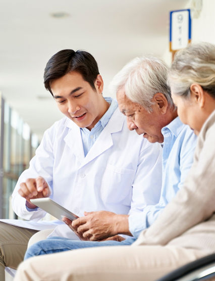 young asian doctor discussing test result and diagnosis with senior couple patients using digital tablet in hospital hallway