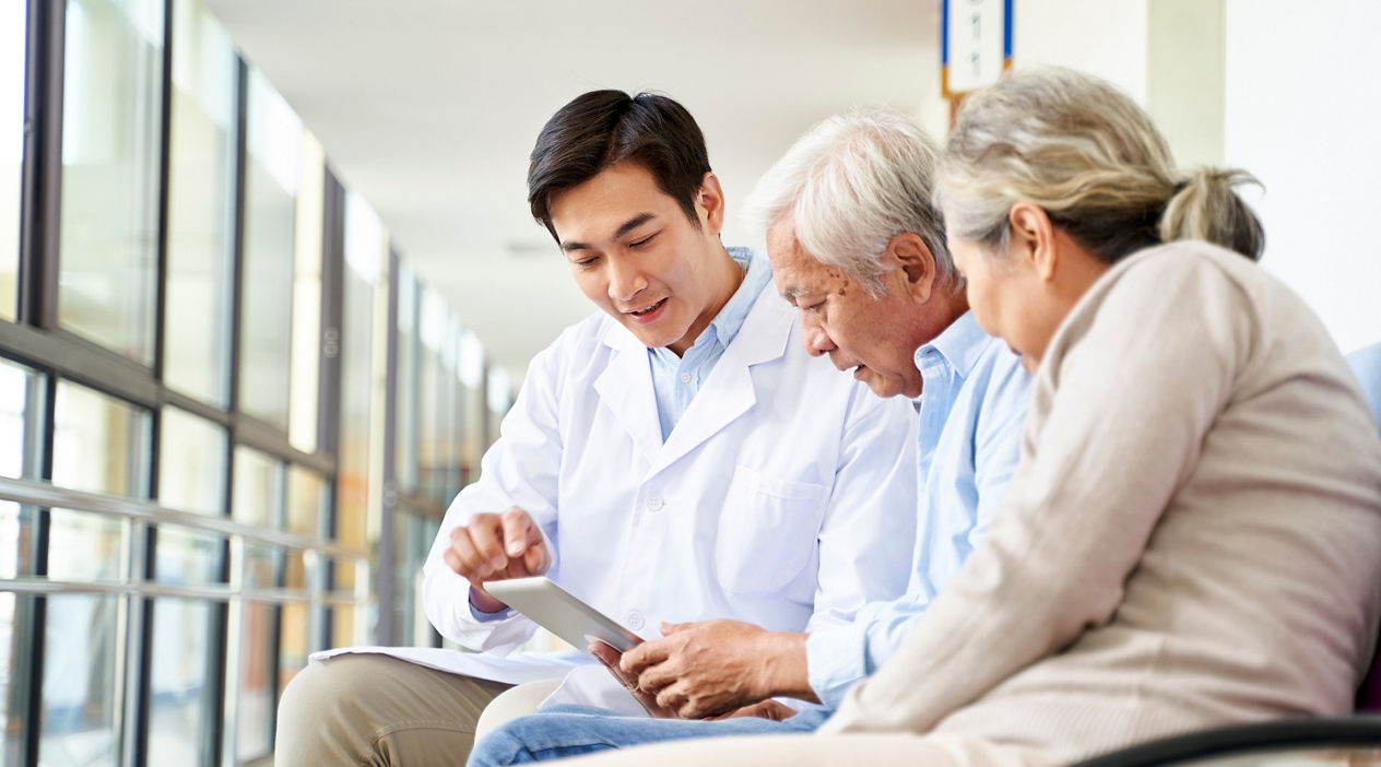 young asian doctor discussing test result and diagnosis with senior couple patients using digital tablet in hospital hallway
