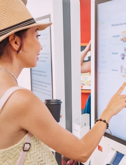A female customer uses a touchscreen terminal or self-service kiosk to order at a fast food restaurant. Automated machine and electronic payment