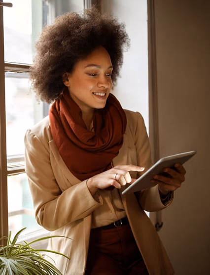 Young Afro-American woman near window on workplace taking information from ipad 