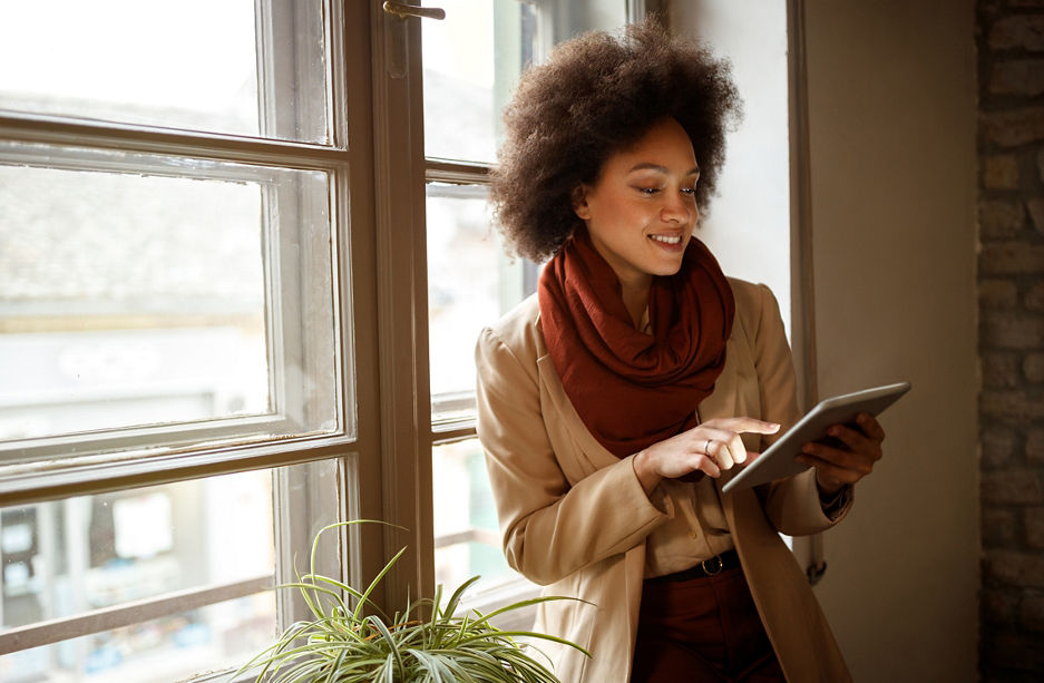 Young Afro-American woman near window on workplace taking information from ipad 