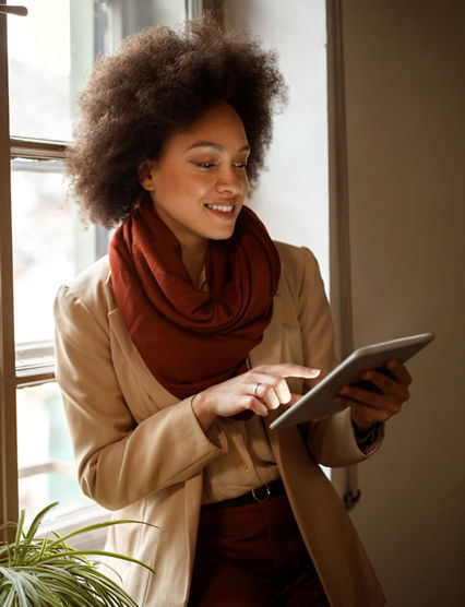 Young Afro-American woman near window on workplace taking information from ipad 