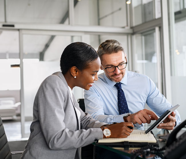 Mature businessman discussing work with black manager writing notes in diary. Confident business man in formal clothing working with african american woman showing data on digital tablet. Smiling professional business people working together on new business strategy.