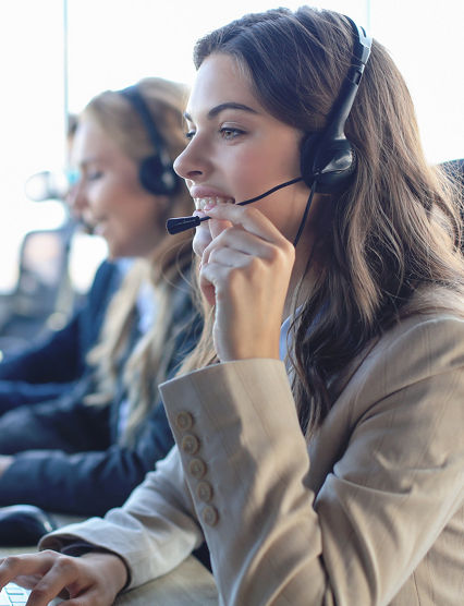 Female customer support operator with headset and smiling, with collegues at background