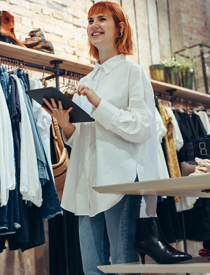 Young shop owner with a digital tablet. Woman working in clothing store with a table pc in hand looking away and smiling.