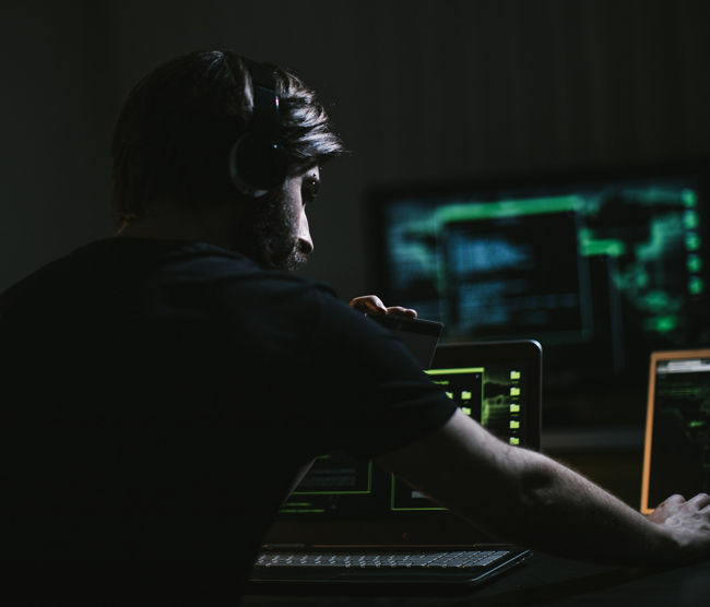 One man, sitting indoors surounded by computers, hacking crime is in motion, holding a credit card.