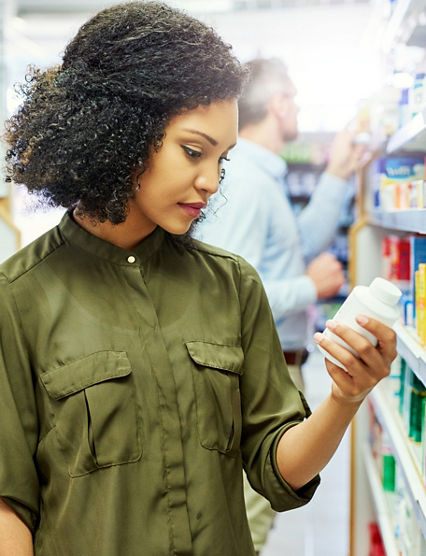 Pharmacy, health shop and woman with medicine for reading label, check product and choice in retail store. African female person looking at drugstore pills for ingredients, information and shopping.