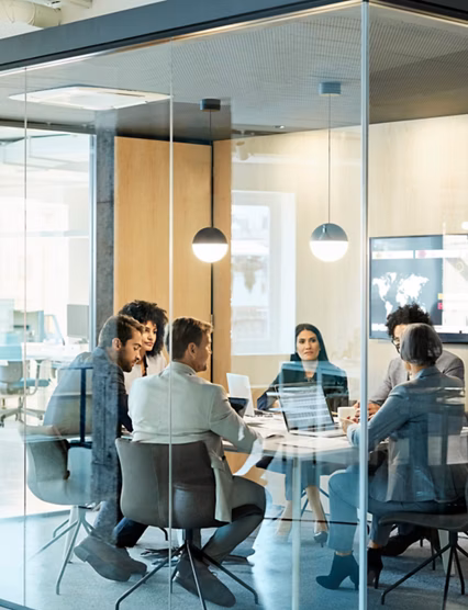 Business colleagues sitting at conference table seen through glass wall. Multi-ethnic coworkers are discussing in board room at office. They are planning strategy.
