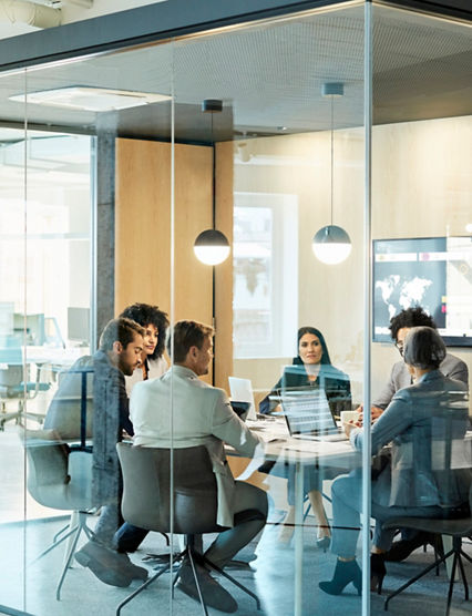 Business colleagues sitting at conference table seen through glass wall. Multi-ethnic coworkers are discussing in board room at office. They are planning strategy.