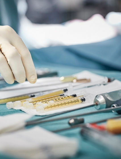 Cropped image of female surgeon reaching for syringes on table. Close-up of healthcare worker's hand wearing surgical glove. She is in emergency room.