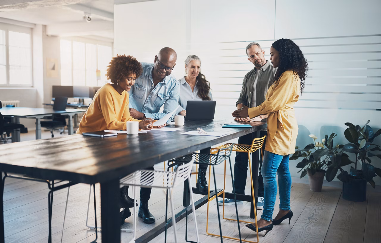 Smiling group of diverse businesspeople talking while working together around a table in a bright modern office