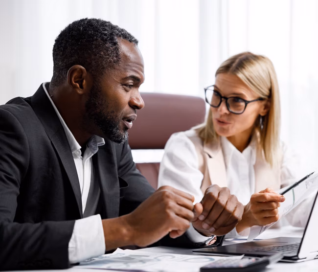 Two people analyze documents on a laptop while sitting at a table in the office. Business partners at work in the office are discussing projects. Multi-racial collaboration
