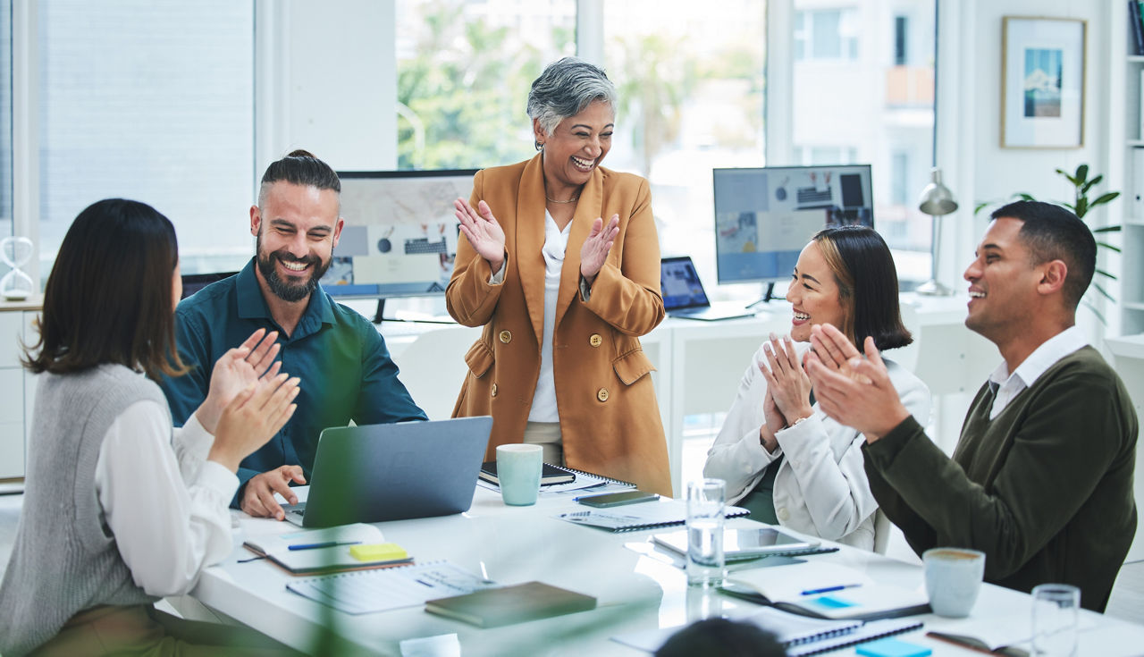 Happy business people in meeting at desk with applause, cheers and celebration of sales target achievement. Clapping, praise and congratulations with success, motivation for men and women in office