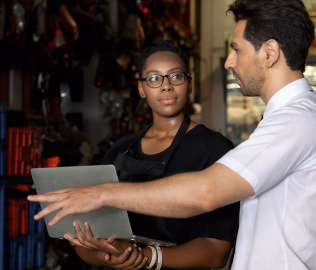 Happy harmony people at workplace, smiling white guy and African American woman working together Two workers check stock at auto spare parts store shop warehouse, surrounded by secondhand engine parts