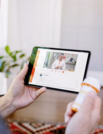 While holding a prescription medication container, an unrecognizable senior man video chats with a female doctor. The man is asking quesitons about his medication.