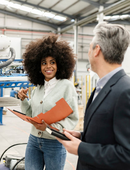 Smiling engineer holding folder discussing with colleague in factory