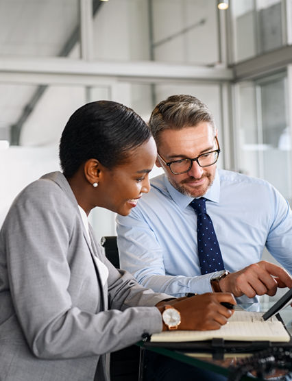 Mature businessman discussing work with black manager writing notes in diary. Confident business man in formal clothing working with african american woman showing data on digital tablet. Smiling professional business people working together on new business strategy.