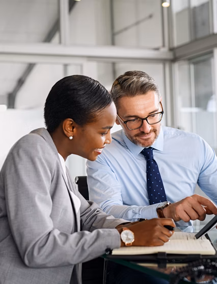 Mature businessman discussing work with black manager writing notes in diary. Confident business man in formal clothing working with african american woman showing data on digital tablet. Smiling professional business people working together on new business strategy.