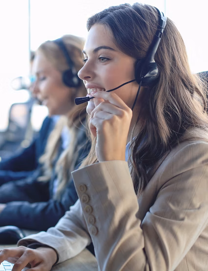 Female customer support operator with headset and smiling, with collegues at background