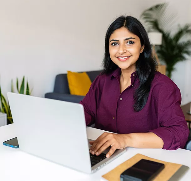 Portrait of cheerful indian business woman smile at camera using laptop at home. Entrepreneur and freelancer people concept.