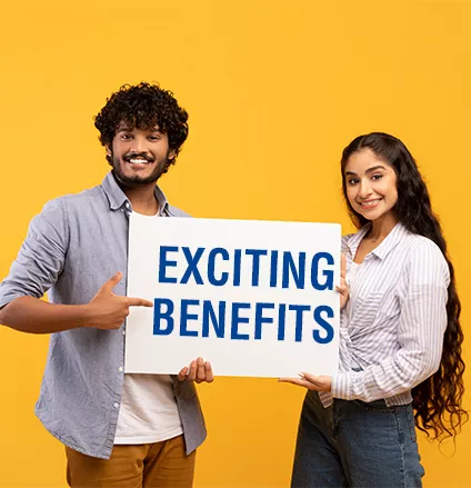 Place for your ad. Portrait of indian couple holding empty blank placard board over yellow studio background. Happy man and woman standing with white paper, pointing at it and smiling at camera