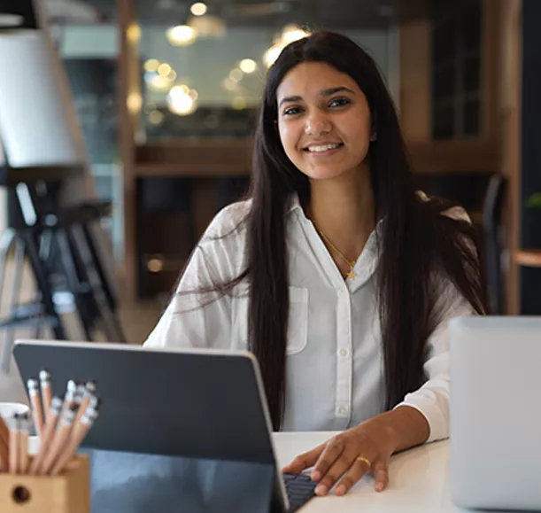 Portrait of female teenager smiling and looking into camera while doing assignment with tablet in library