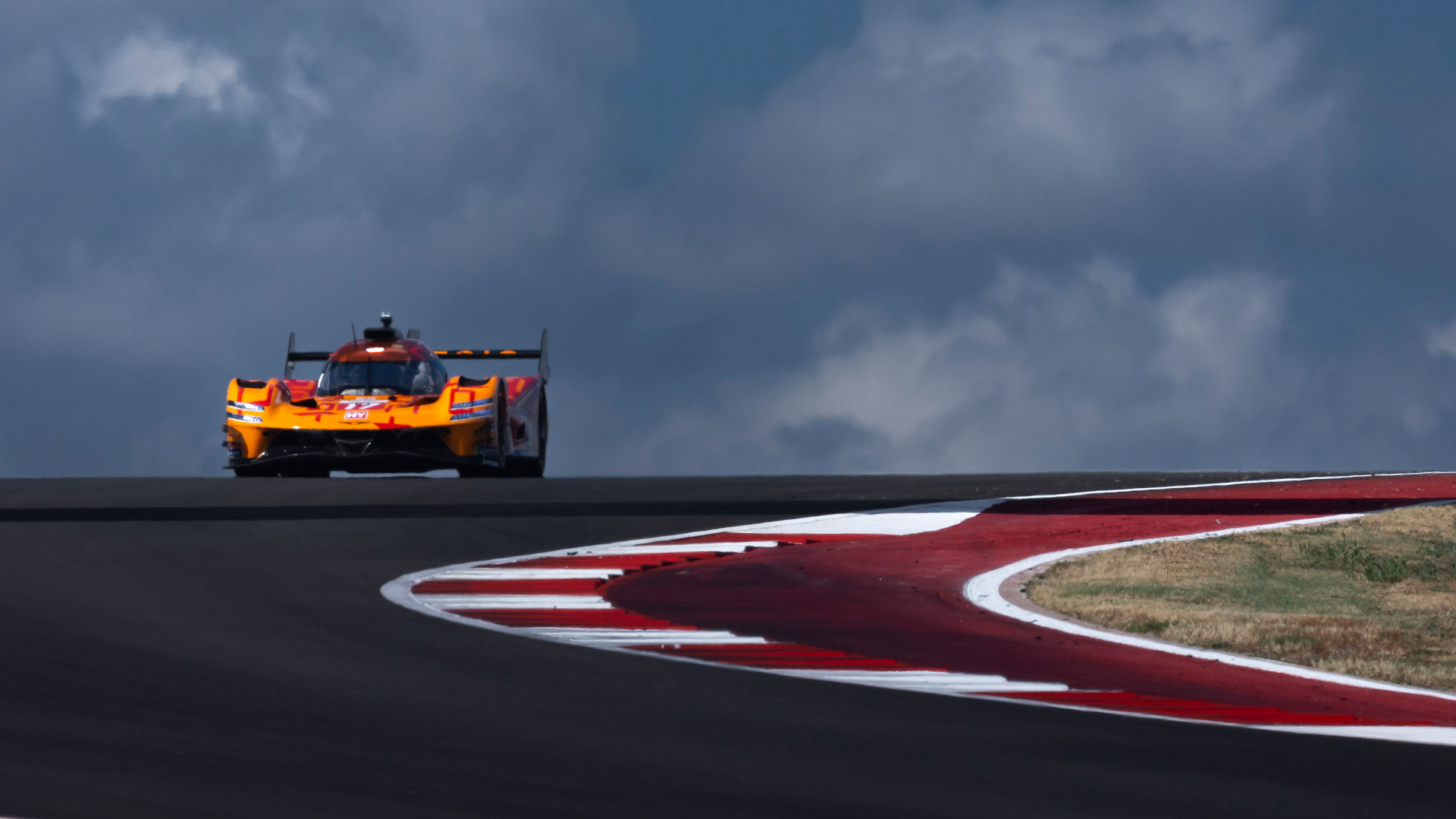 Genesis GMR-001 crests a hill at COTA under dramatic Texas skies during Lone Star Le Mans.