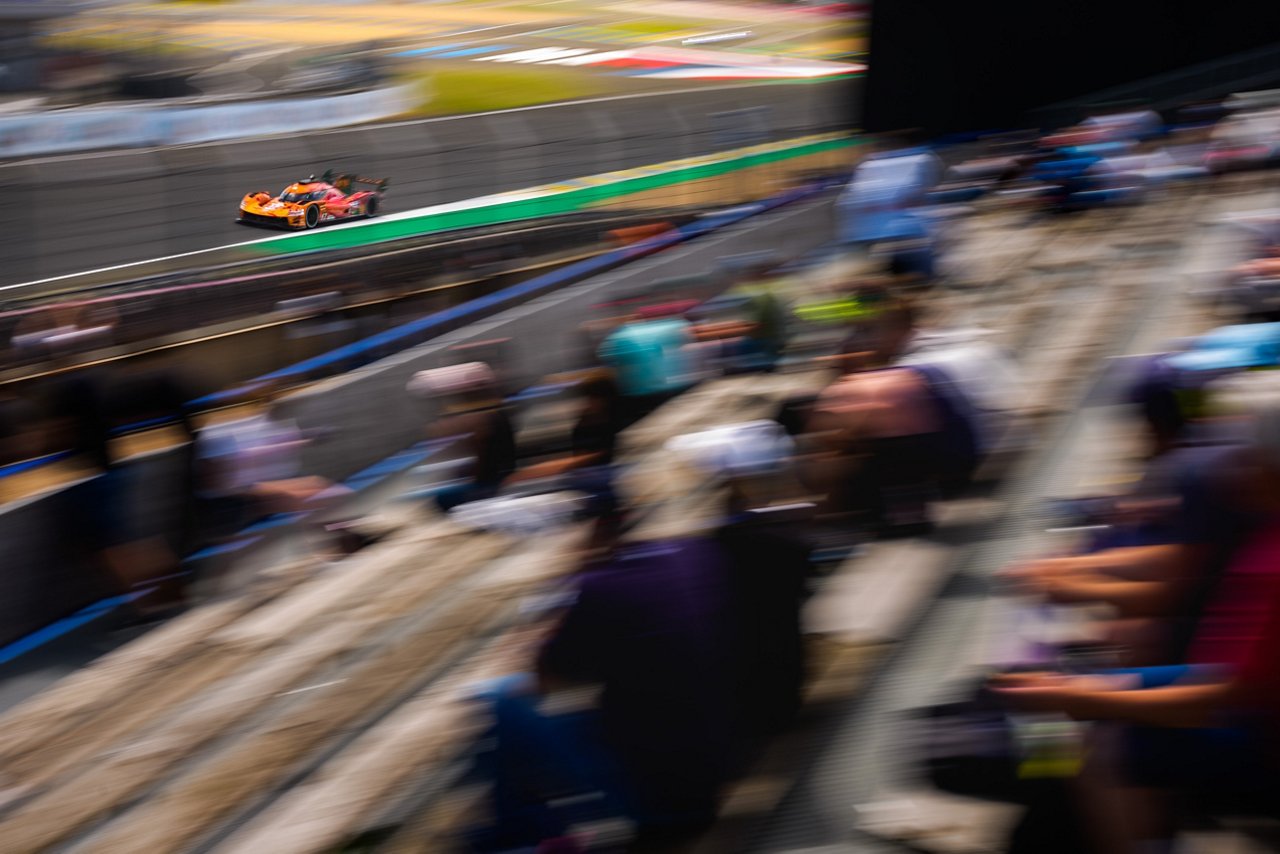 Blurred panning shot of the Genesis GRM-001 speeding past a racetrack grandstand with spectators.