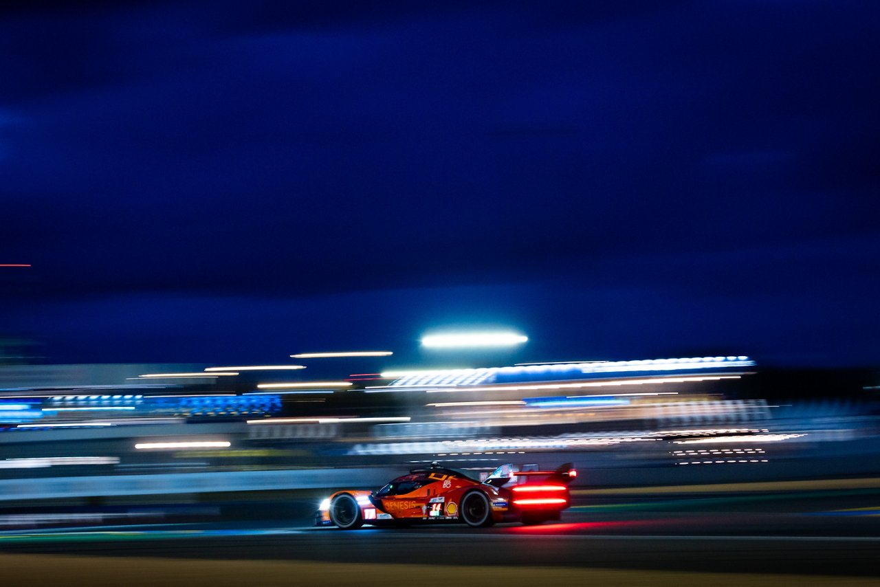 Genesis GRM-001 racing at night, taillights glowing red and background lights blurred into streaks.