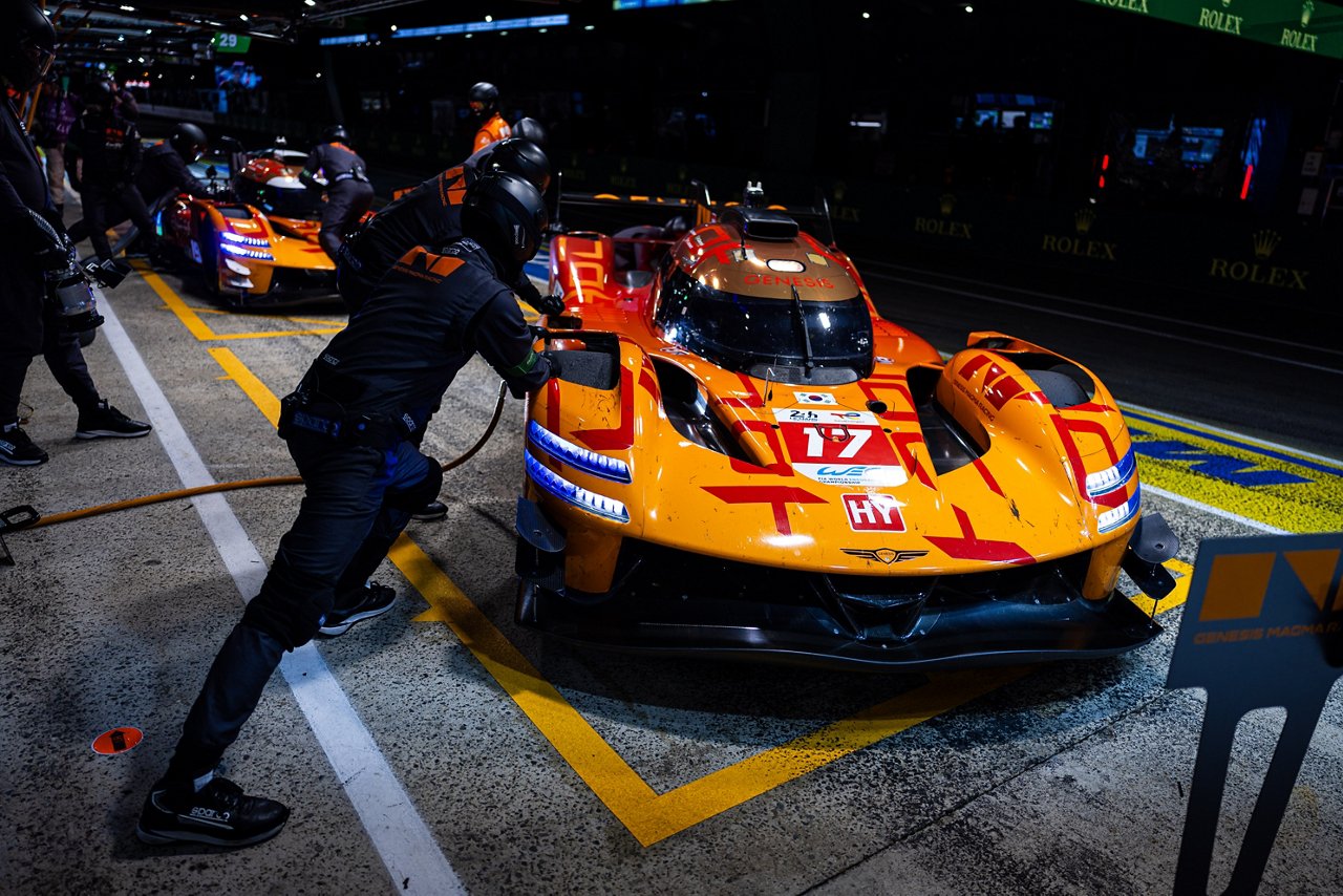 Genesis GRM-001 in the pit lane at night while crew members refuel and service the car during a stop.