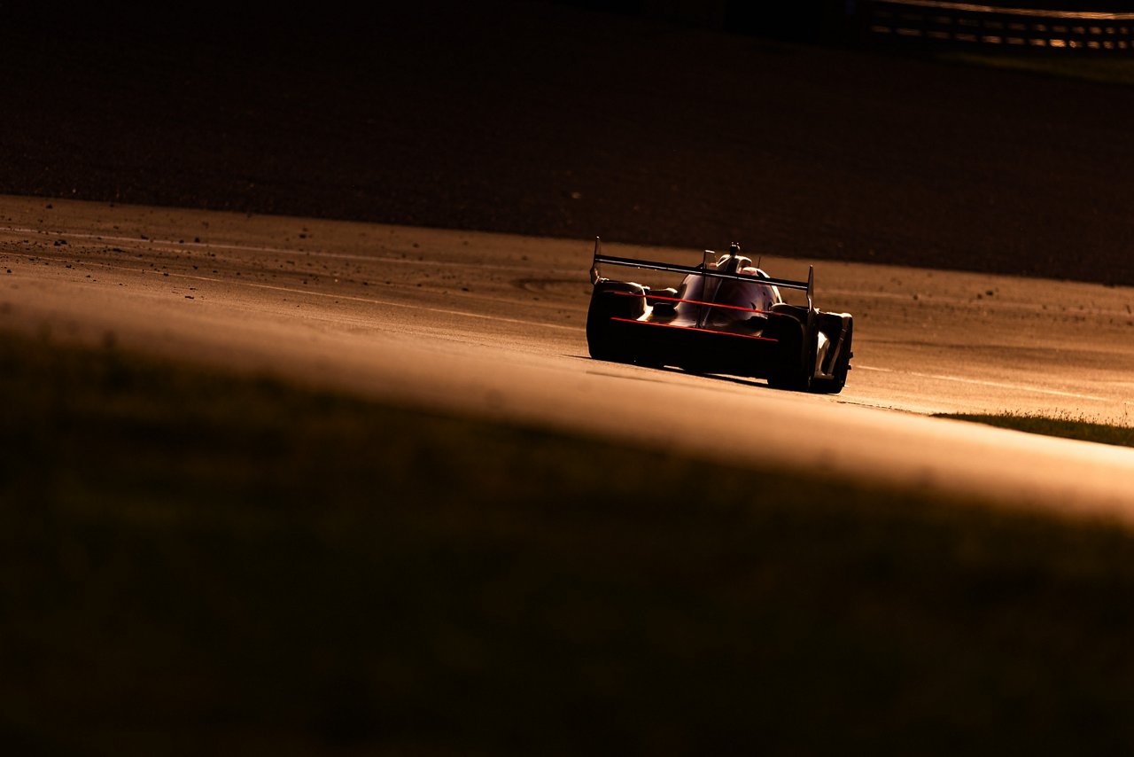 GRM-001 speeding along the track at dusk, rear lights glowing red in warm sunset light.