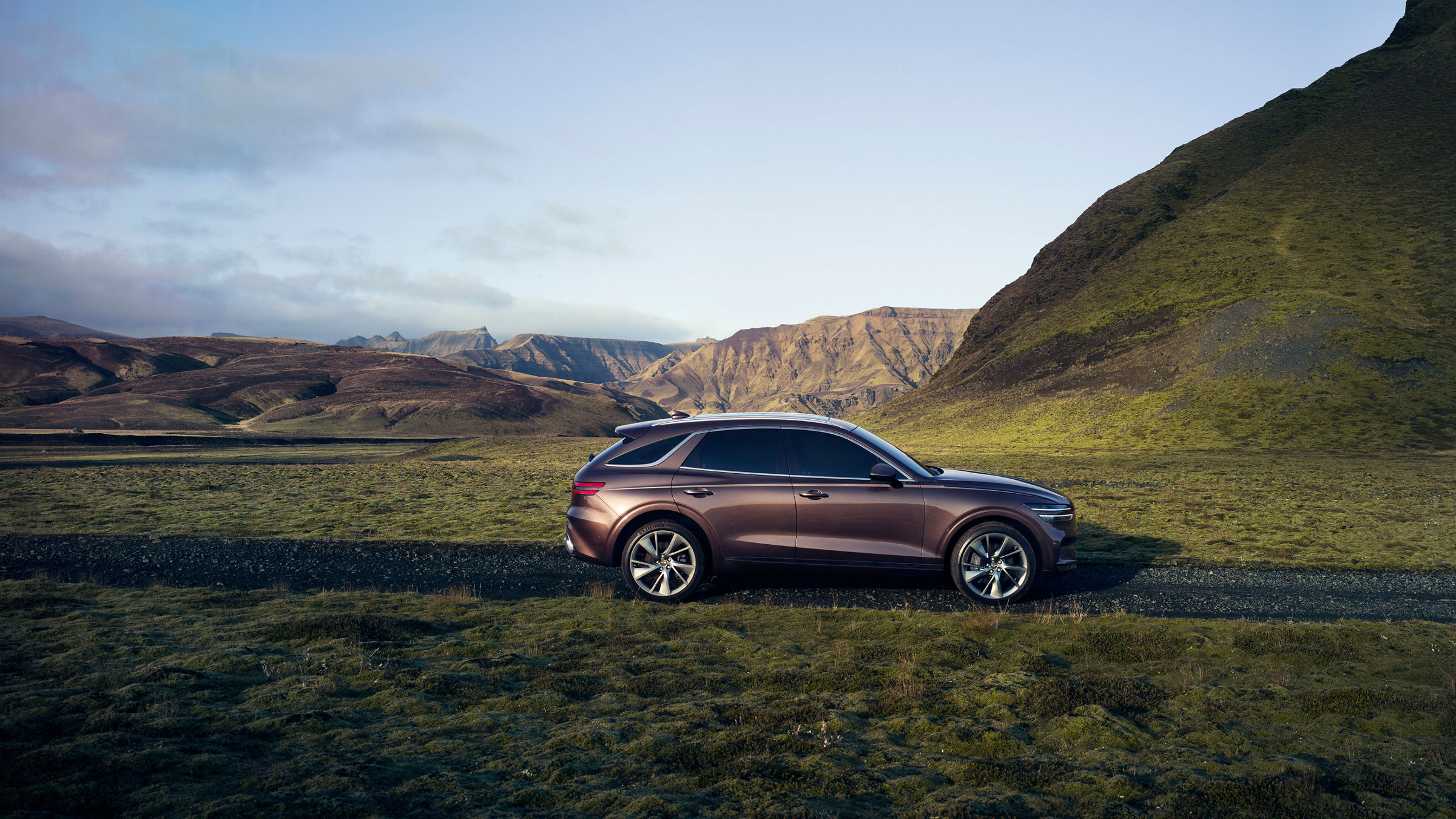 Genesis GV70 Burgundy from the side on a road in front of some Mountains