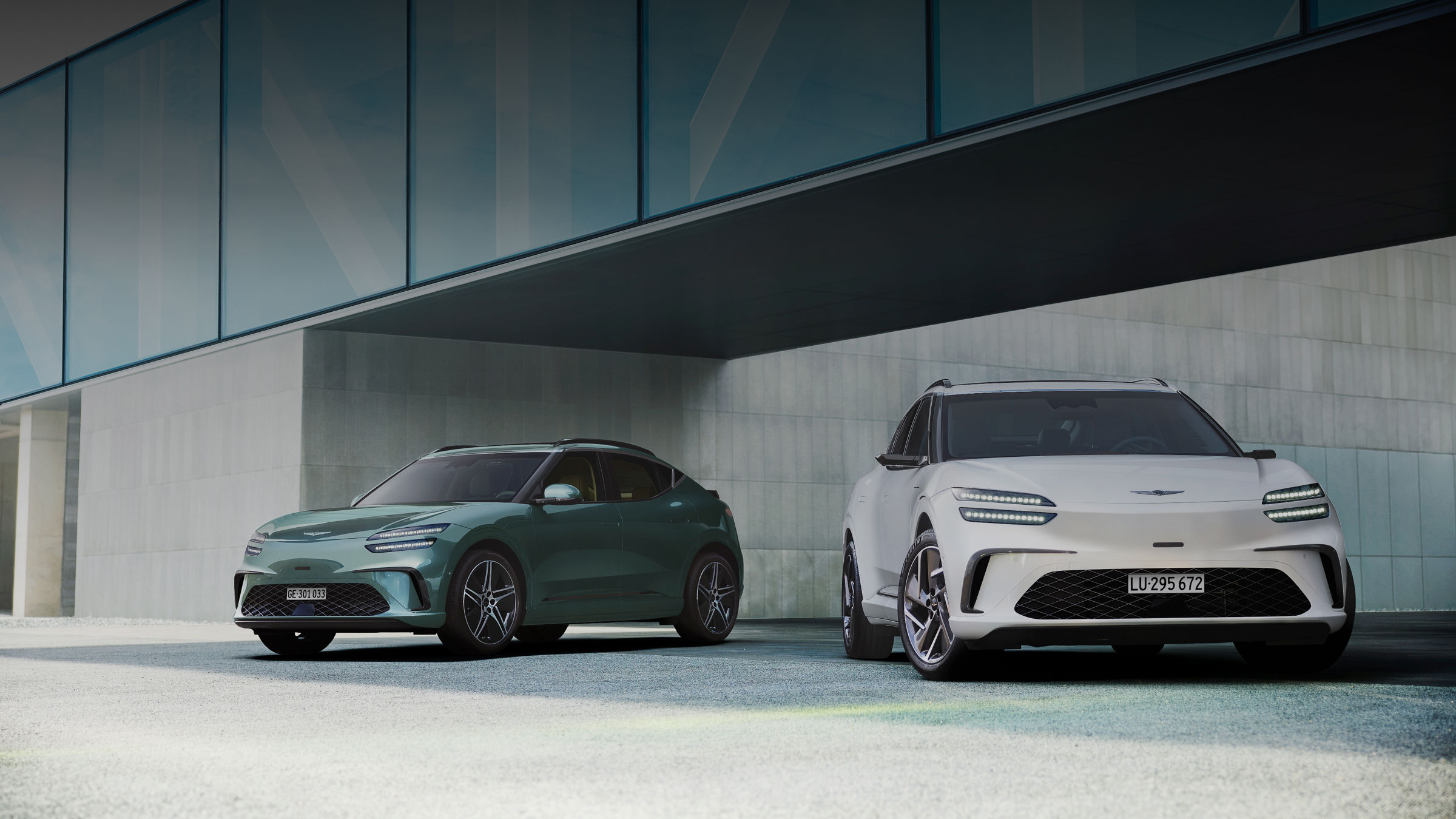  Vor dem Hintergrund des modernen Gebäudes steht links ein GV60 in Tromsø-Grün und rechts ein GV60 in Uyuni-Weiß.